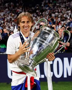 a man holding up a soccer trophy in front of a large group of people on the field