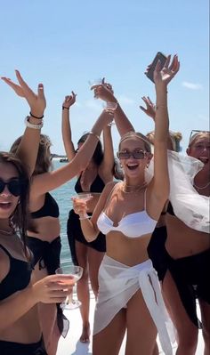 several women in bathing suits are posing on the beach with their hands up and holding wine glasses