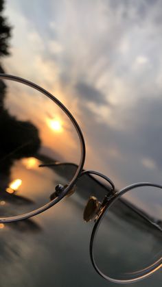 a pair of glasses sitting on top of a table next to the ocean at sunset