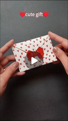 two hands holding an origami envelope with red hearts and a bow on it