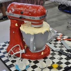 a red mixer sitting on top of a black and white checkered table