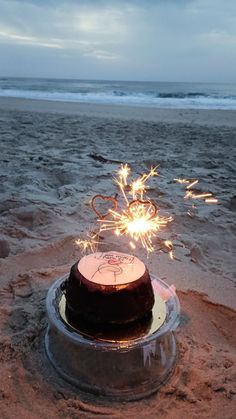 a birthday cake on the beach with sparklers sticking out of it's top