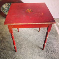 an old red wooden table sitting on top of a carpeted floor next to a mirror