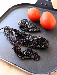 two tomatoes and some black pepper on a pan with food in the bottom right corner