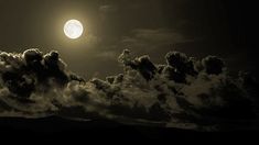 the full moon is shining brightly in the night sky above clouds and mountains on a dark, cloudy day