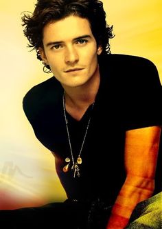 a young man with curly hair wearing a black t - shirt and silver chain necklace