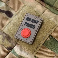 a red button that says do not press on the back of a camouflage uniform pocket