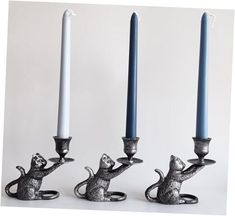 three silver candlesticks with cats on them and one holding a candle holder in the shape of a mouse