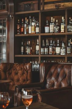 a leather couch sitting in front of a wooden shelf filled with bottles and wine glasses