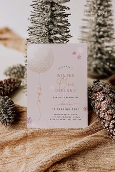 a pink and gold winter onederland party with pine cones, snowflakes, and cards