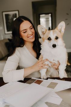 a woman sitting at a table with a dog in her lap and papers around her