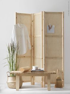 a room divider made out of bamboo with a plant in the corner and a white shirt hanging on it