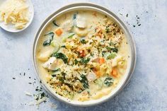 a bowl filled with pasta and vegetables on top of a blue surface next to a spoon