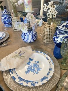 a blue and white dinner table setting with flowers in vases, plates and napkins