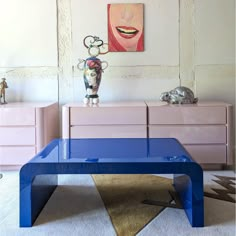 a blue coffee table sitting in front of a painting on the wall next to dressers