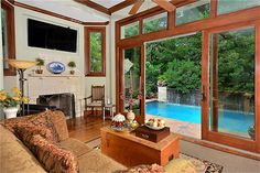 a living room filled with furniture and a fire place next to a swimming pool on top of a wooden floor