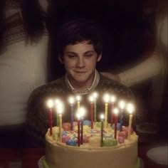 a man sitting in front of a birthday cake with lit candles on top of it