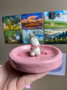 a small toy rabbit sitting on top of a pink object in front of some pictures