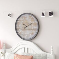 a clock on the wall above a bed with pink pillows and throw pillows in front of it