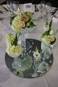 three glass vases filled with flowers and greenery on a silver platter at a wedding reception