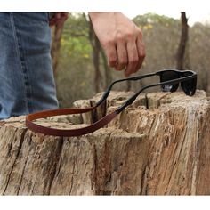 a pair of glasses being held by a man on top of a tree stump in the woods