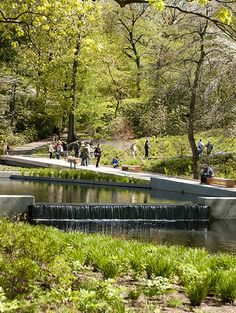 people are walking around in the park near a small pond and waterfall with water running through it