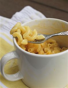 a spoon full of macaroni and cheese in a white cup on a yellow towel