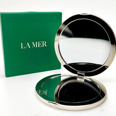 a compact mirror sitting on top of a table next to a green box that says la mer