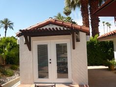 a small white building with a bench in front of it and palm trees behind it