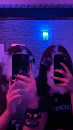 two people taking pictures with their cell phones in front of a brick wall and neon lights