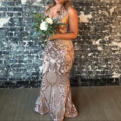 a woman standing in front of a brick wall holding a bouquet of flowers and looking at the camera