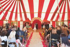 a large red and white striped tent with people sitting in chairs at the end of it