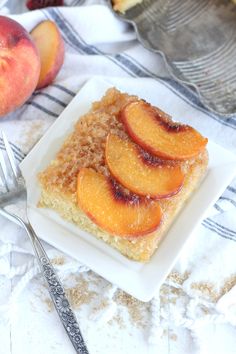 a slice of cake with sliced peaches on top sitting on a plate next to a fork