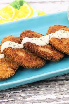 some fried food on a blue plate with sauce and lemon wedges next to it