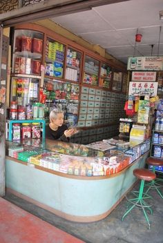 a man reading a newspaper in front of a store with many items on the counter