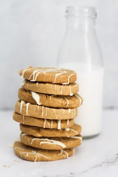 a stack of cookies with icing on top next to a bottle of milk and a glass of milk