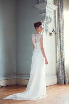 a woman in a white wedding dress standing by a window