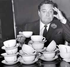 a black and white photo of a man sitting at a table full of tea cups