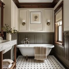 a white bath tub sitting under a window next to a sink and a wooden framed mirror