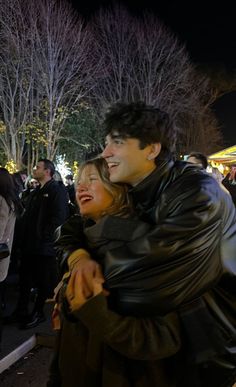 a man and woman hugging each other in front of a group of people at night