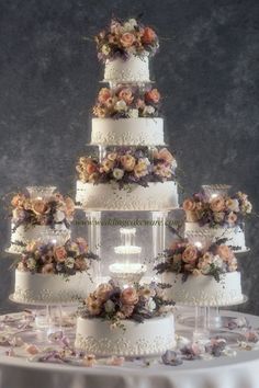 a three tiered wedding cake with flowers on the top and bottom is surrounded by wine glasses