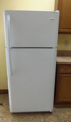 a white refrigerator freezer sitting on top of a kitchen floor next to wooden cabinets