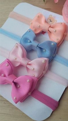 four small bows with pearls on them sitting on top of a white and pink striped cloth