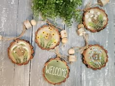 four wood slices with flowers and welcome signs on them, hanging from twine strings