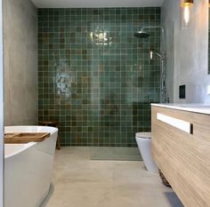 a modern bathroom with green tile on the walls and floor, along with a white bathtub