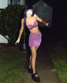 a woman with purple hair and makeup is walking down the sidewalk wearing a short skirt