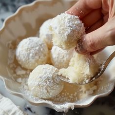 a hand holding a spoon with powdered sugar on top of it in a bowl