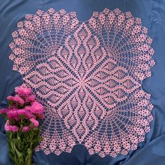 pink crocheted doily next to purple flowers on blue satin sheet with white background