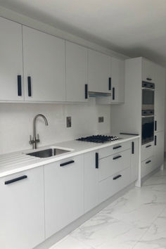 an empty kitchen with white cabinets and marble counter tops, including a stainless steel sink