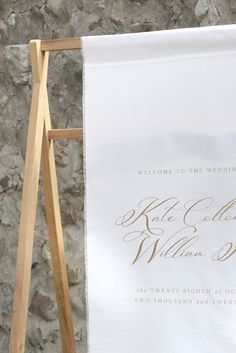 a wedding welcome sign hanging on a wooden easel next to a stone wall,